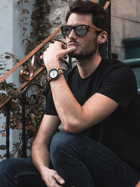 Homme assis en ville portant lunettes de soleil et montre en bois The Wood Stock