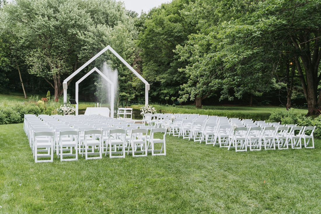 Cérémonie de mariage en extérieur : rangées de chaises blanches et arche face à un bassin