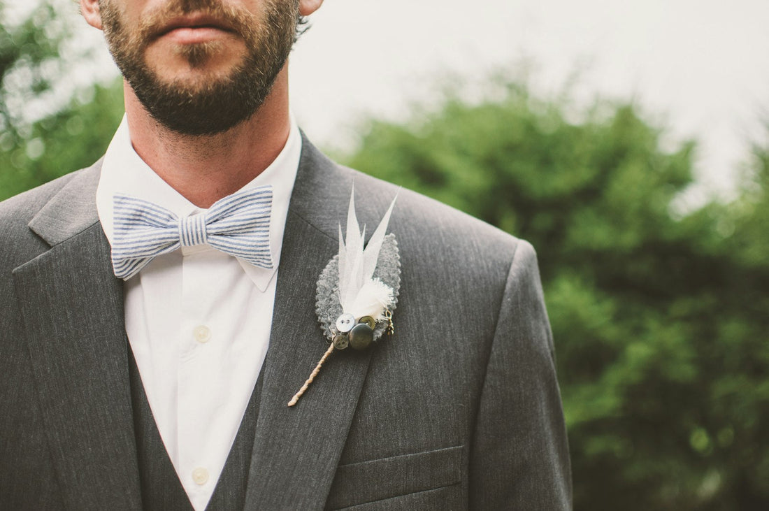 Homme en costume gris avec un nœud papillon rayé et une boutonnière, le jour d'un mariage