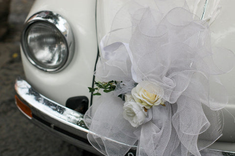 Gros nœud en tulle blanc et roses fixé à l'avant d'une voiture de mariage